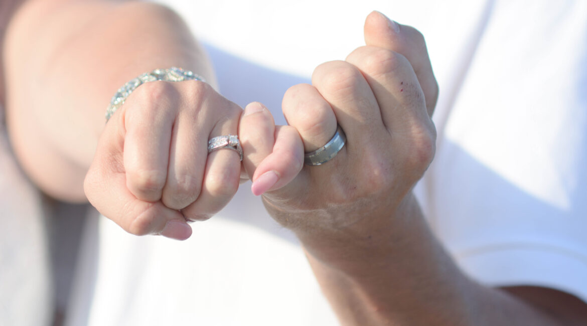 Couple linking pinky fingers with wedding rings